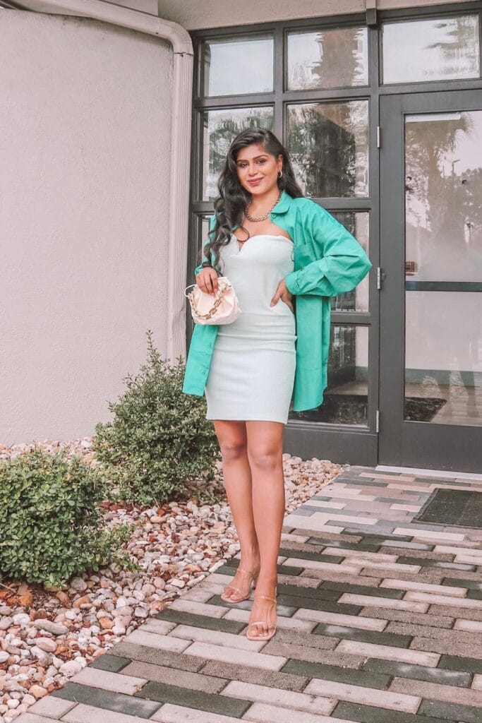 How To Style Oversized Shirts Like A Fashion Blogger 17 Woman Standing Confidently In Front Of A Modern Entrance, Wearing A Mint Green Oversized Shirt Over A Light Blue Dress, Holding A Small Handbag.