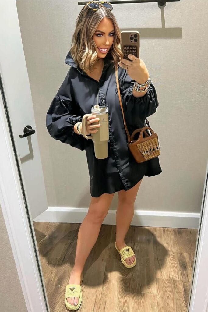 How To Style Oversized Shirts Like A Fashion Blogger 12 Woman In A Black Oversized Shirt Dress, Holding A Tumbler And A Handbag, Smiling In A Mirror Selfie.