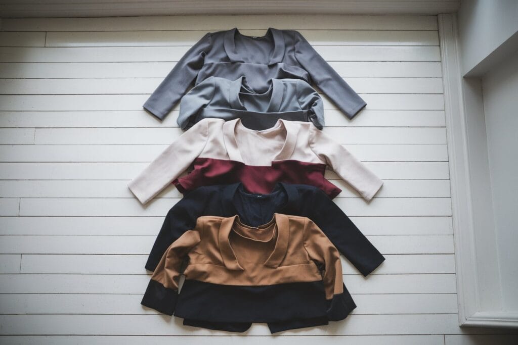 How To Layer Clothes Like A Fashion Pro 3 Flat Lay Composition Showing Three Complete Layered Outfits Arranged Vertically, Each Demonstrating A Different Color Strategy: Top Outfit In Monochromatic Grays, Middle Outfit With Neutral Base Plus One Burgundy Accent Piece, Bottom Outfit In Complementary Navy And Camel Tones. Shot From Directly Above, Items Neatly Arranged, White Oak Wooden Floor Background, Natural Window Lighting, Styled With Minimal Accessories, Pinterest-Worthy Aesthetic, Professional Styling Photography